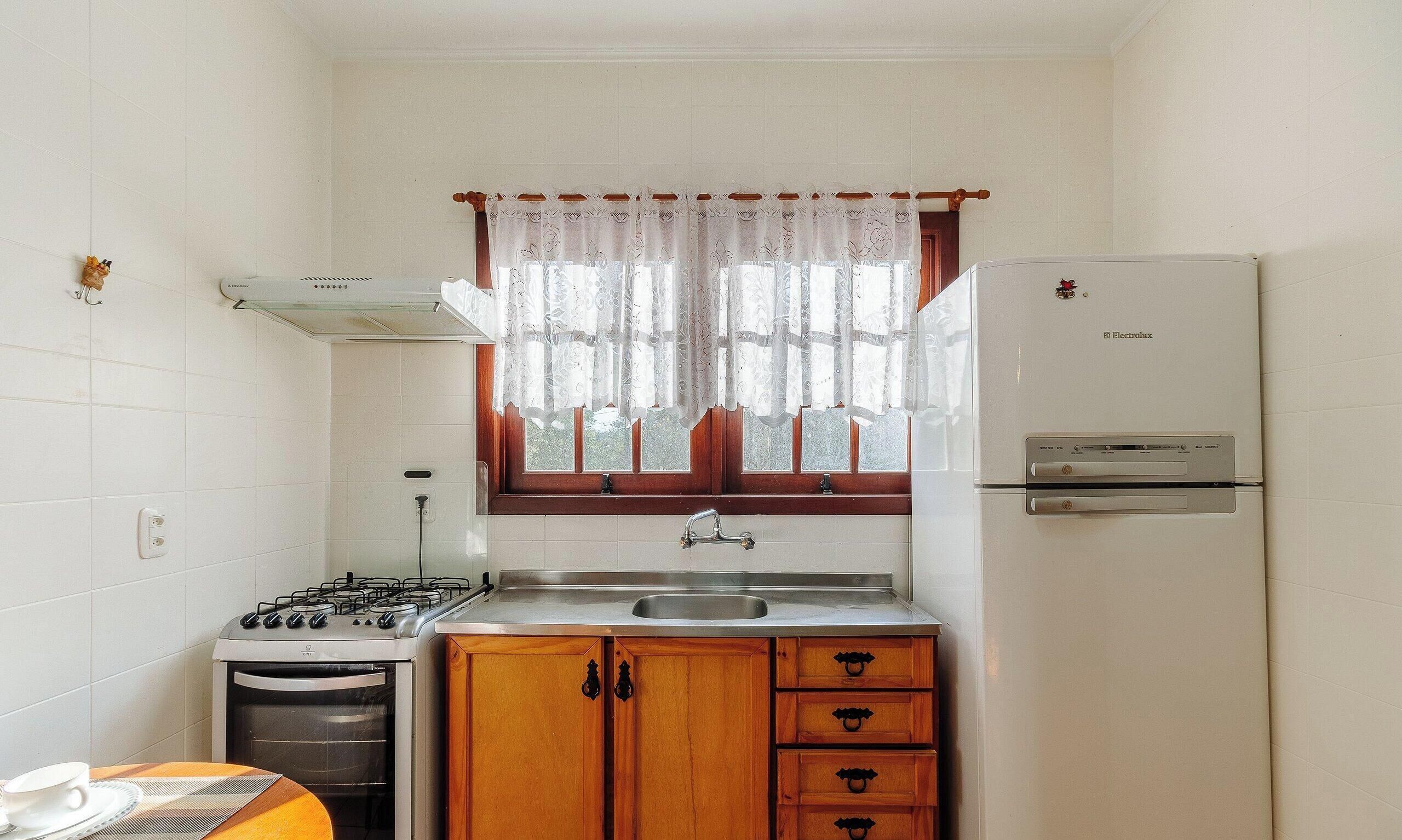 A compact kitchen with a gas stove, oven, sink, wooden cabinets, and a refrigerator.