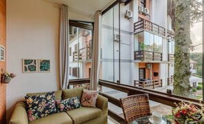 A balcony with a wicker chair, a table with a cup, and a view of a building with balconies. - Apt Duplex With Fireplace in Gramado Rln204 (Gramado)
