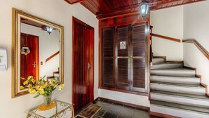 A staircase with wooden steps and a handrail, a wooden door with a mirror and a wreath, and a glass table with a vase of flowers. - Charming Apt in the Heart of Gramado! Rln0105 (Gramado)