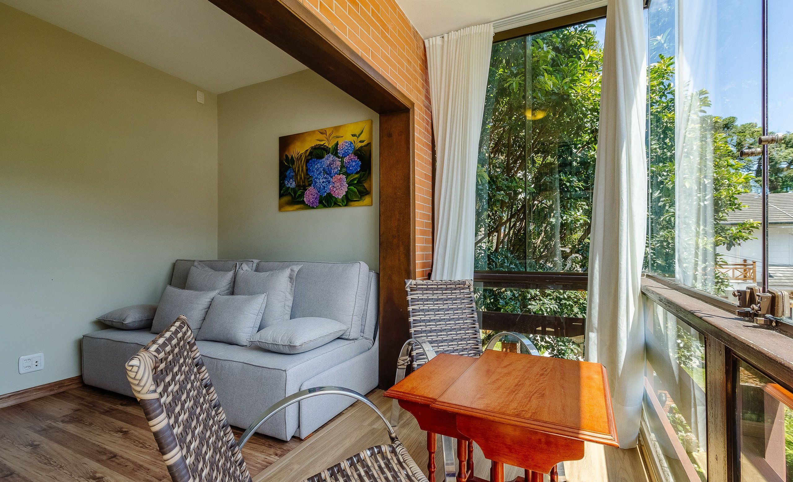 A balcony with a wooden table and chairs, a grey sofa, and a painting on the wall.