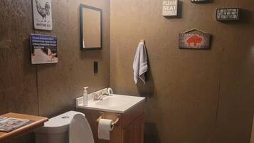 Un baño pequeño con inodoro, lavabo y espejo. Hay varios carteles en las paredes, incluyendo uno que dice 'I can't adult today'.