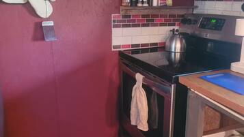 Une cuisine de taille réduite avec un mur rouge, une cuisinière en acier inoxydable et un pare-feu en carreaux.