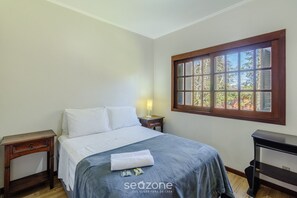 Une chambre à coucher comprenant un lit, une table de chevet, une lampe, une fenêtre avec des stores et un bureau.
