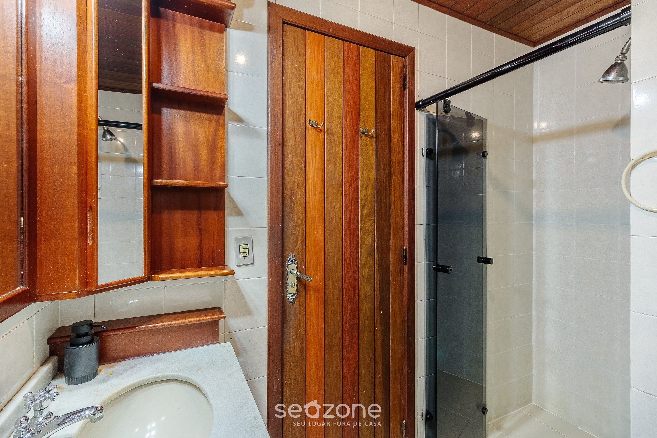 Un baño con tocador de madera, un espejo, un lavamanos y una zona de ducha.