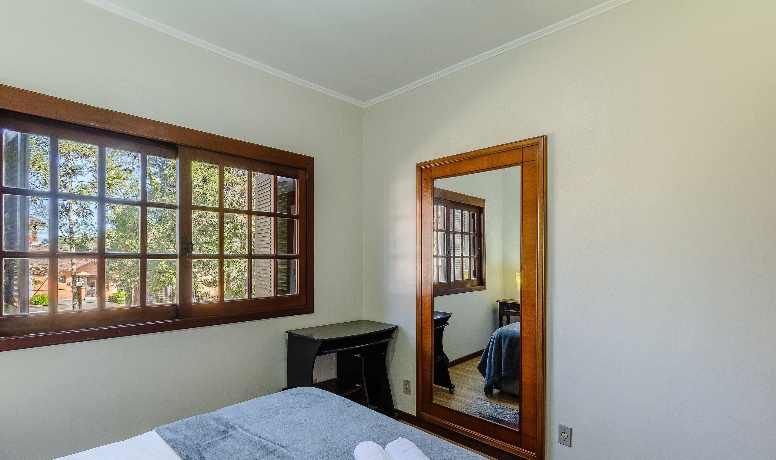 A bedroom with a large window, a mirror, a bed, and a small desk.