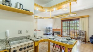 Une cuisine compacte équipée d’une cuisinière à gaz, d’une machine à café et d’un four à micro-ondes. On y trouve un coin repas avec une table pour deux personnes, ainsi qu’une chaise dotée d’un coussin à motifs zébrés.
