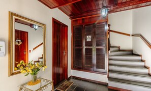 Un escalier avec des marches en bois et une rampe, une porte en bois ornée d’un miroir et d’une guirlande, et une table en verre sur laquelle est posé un vase de fleurs.