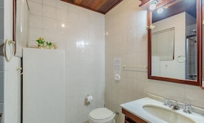 Een badkamer met witte tegels, een toilet, een wastafel met spiegel en een handdoekhouder.