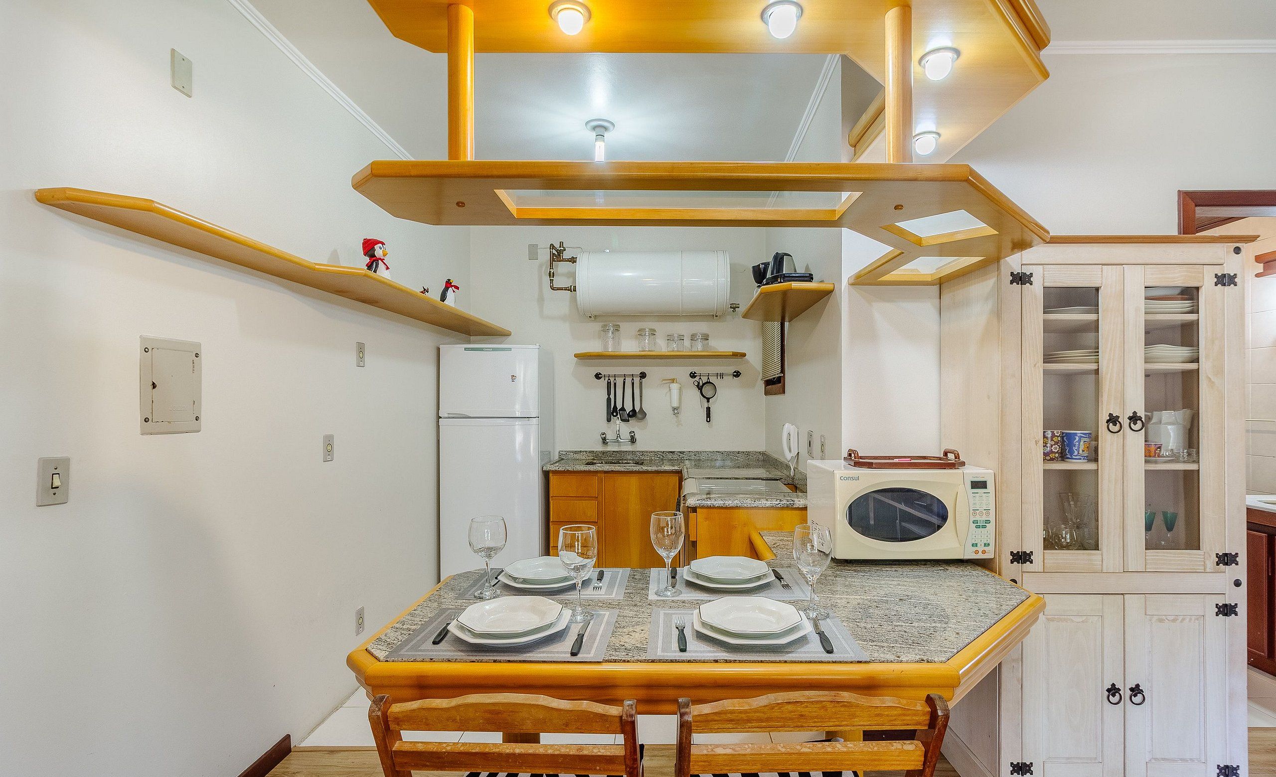 Un coin repas avec une table en bois dressée pour quatre personnes, une cuisine en arrière-plan et un meuble avec des portes en verre.