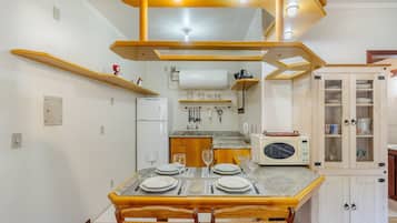 A dining area with a wooden table set for four, a kitchen in the background, and a cabinet with glass doors.