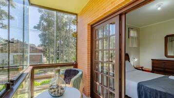 A bedroom with a large window, a balcony, and a bed with a blue bedspread.