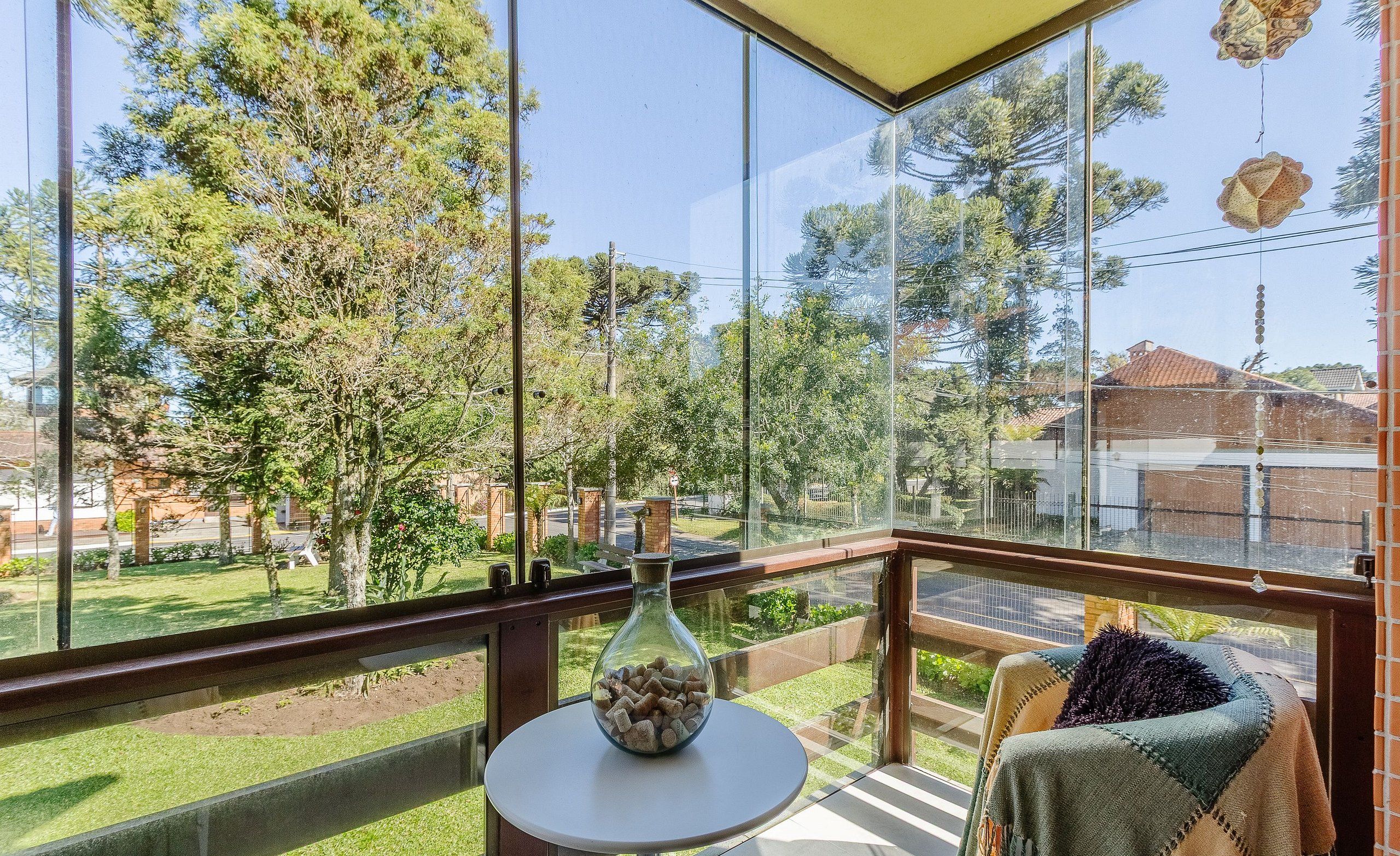 A balcony with a glass railing, a small table with a vase, and a blanket draped over a chair.