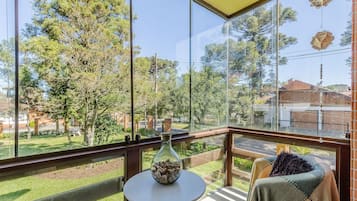 A balcony with a glass railing, a small table with a vase, and a blanket draped over a chair.