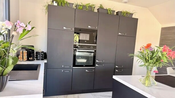 A modern kitchen with dark cabinetry, an oven, and a countertop. - Villa Zinga—Pool, Garden, and Absolute Peace and Quiet (Béziers)