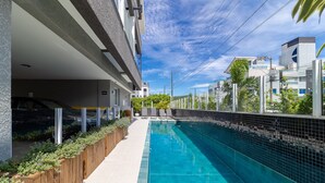 A modern building with a swimming pool, a covered parking area, and a view of neighboring buildings. - Modern apt With Pool and hot Tub! Rhl0305 (Florianópolis)