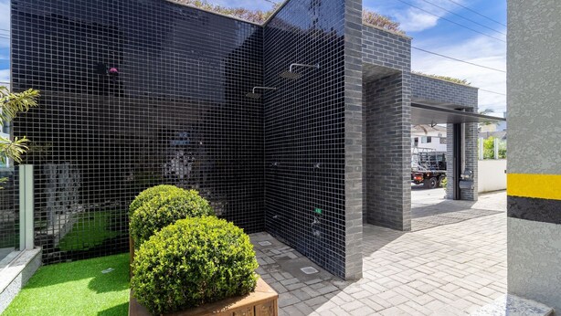 A modern building with a black tiled exterior, a small green lawn, and a wooden planter. - Modern apt With Pool and hot Tub! Rhl0305 (Florianópolis)