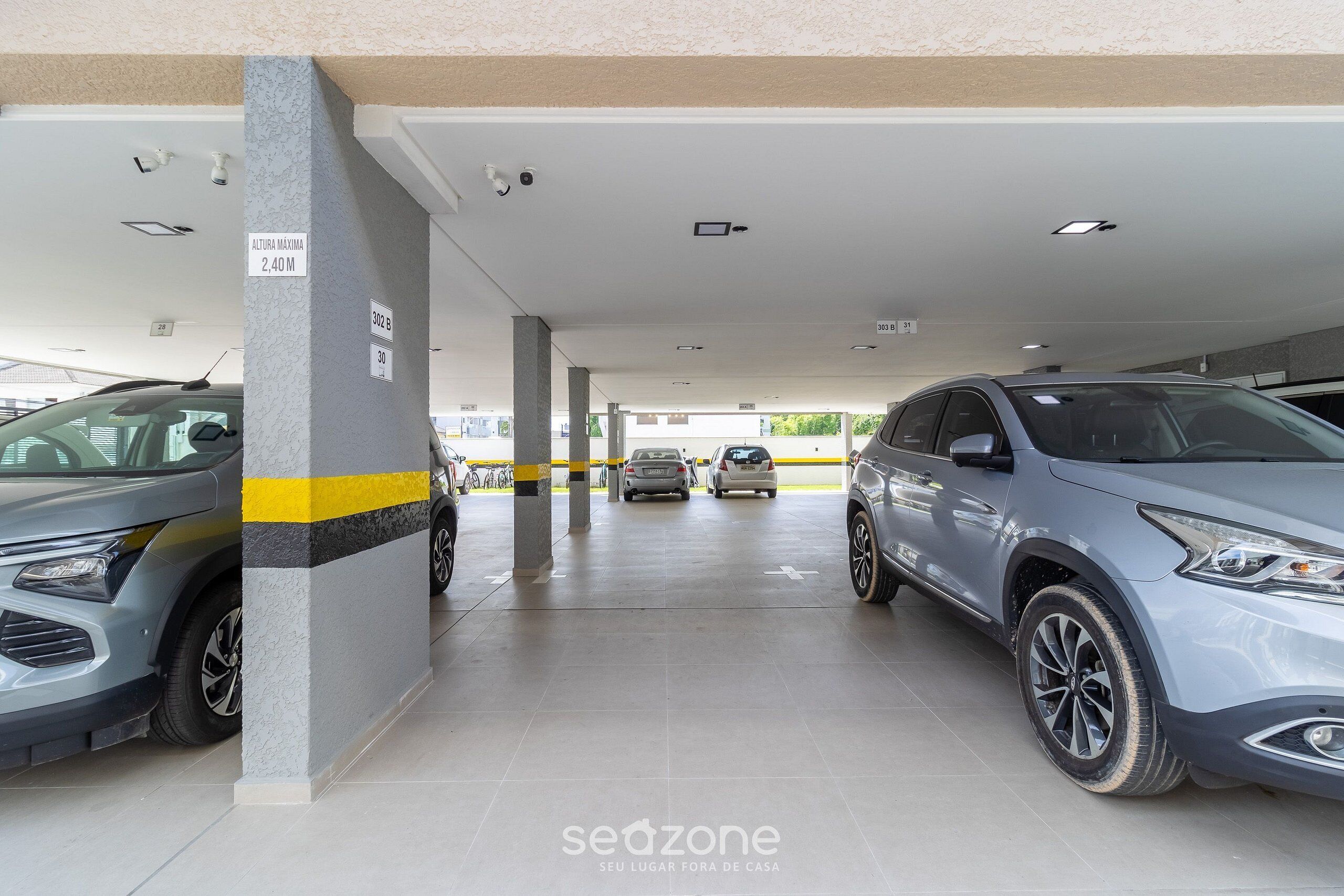 A parking garage with multiple cars parked, ceiling lights, and pillars with height restriction signs.