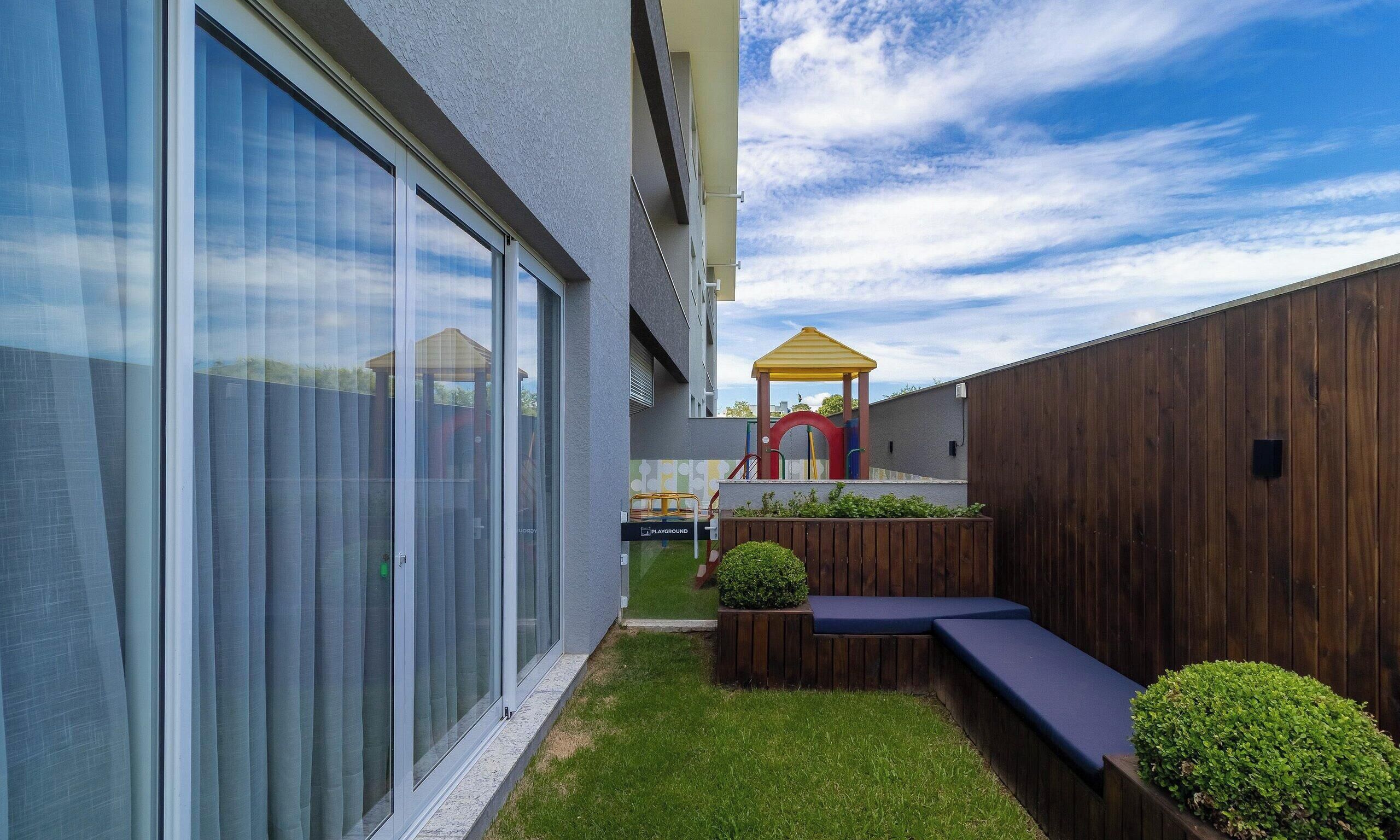 A modern outdoor area with a play structure, a wooden bench, and a planter with greenery.