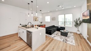 Una cocina moderna con una isla central, una zona de comedor con sofá negro y una sala de estar con sofá negro y una mesita de centro.