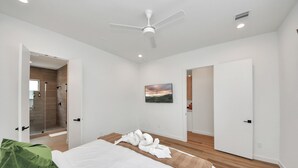 Un dormitorio moderno con cama, ventilador de techo, ducha y un cuadro en la pared.
