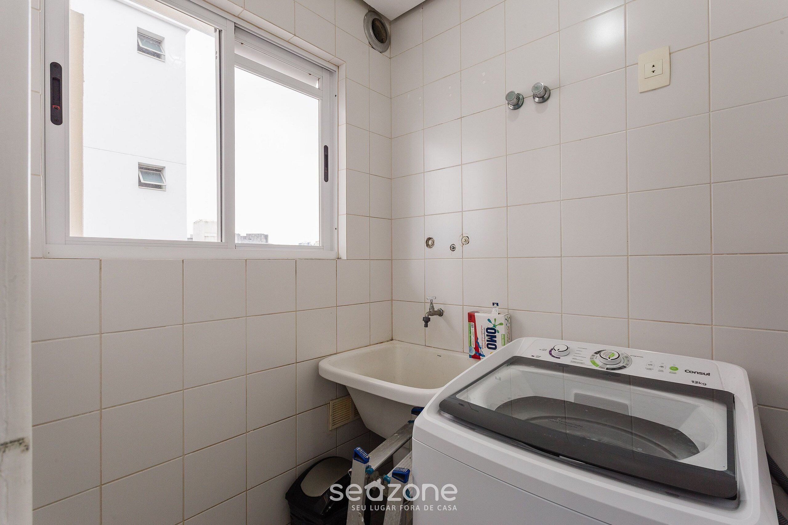 A small bathroom with a window, a sink, and a washing machine.