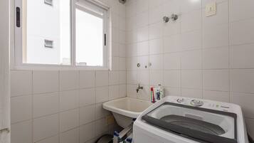 A small bathroom with a window, a sink, and a washing machine.