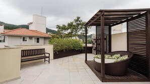 A rooftop patio with a wooden pergola, a wicker chair with cushions, a bench, and a tiled floor. - Penthouse With Private Pool and Barbecue Rgp302 (Florianópolis)