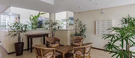 Un amplio salón con mobiliario de mimbre, ventanas grandes y plantas en macetas.