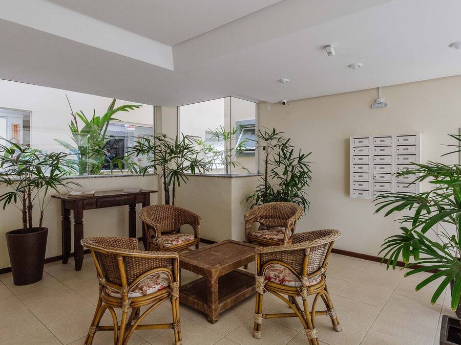 Un amplio salón con mobiliario de mimbre, ventanas grandes y plantas en macetas.