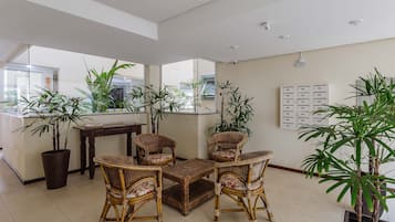 A spacious living area with wicker furniture, large windows, and potted plants.
