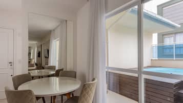 A modern dining area with a glass table and cushioned chairs, a large mirror, and a view of a swimming pool and outdoor space.