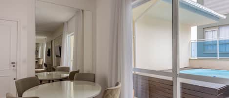 A modern dining area with a glass table and cushioned chairs, a large mirror, and a view of a swimming pool and outdoor space.