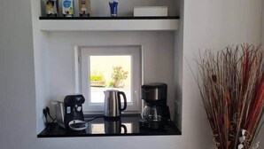 A compact kitchen with a window, a coffee maker, a kettle, and a vase with dried plants.