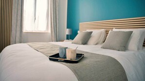 A neatly made bed with a tray of breakfast items, a bedside lamp, and a window with curtains.