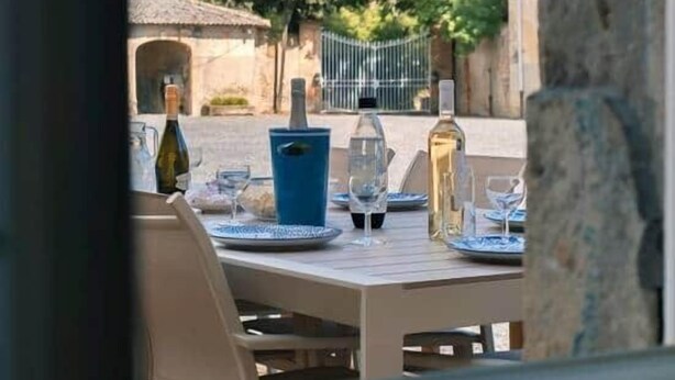An outdoor dining area with a table set for two, featuring a bottle of wine, a glass, and a blue pitcher.