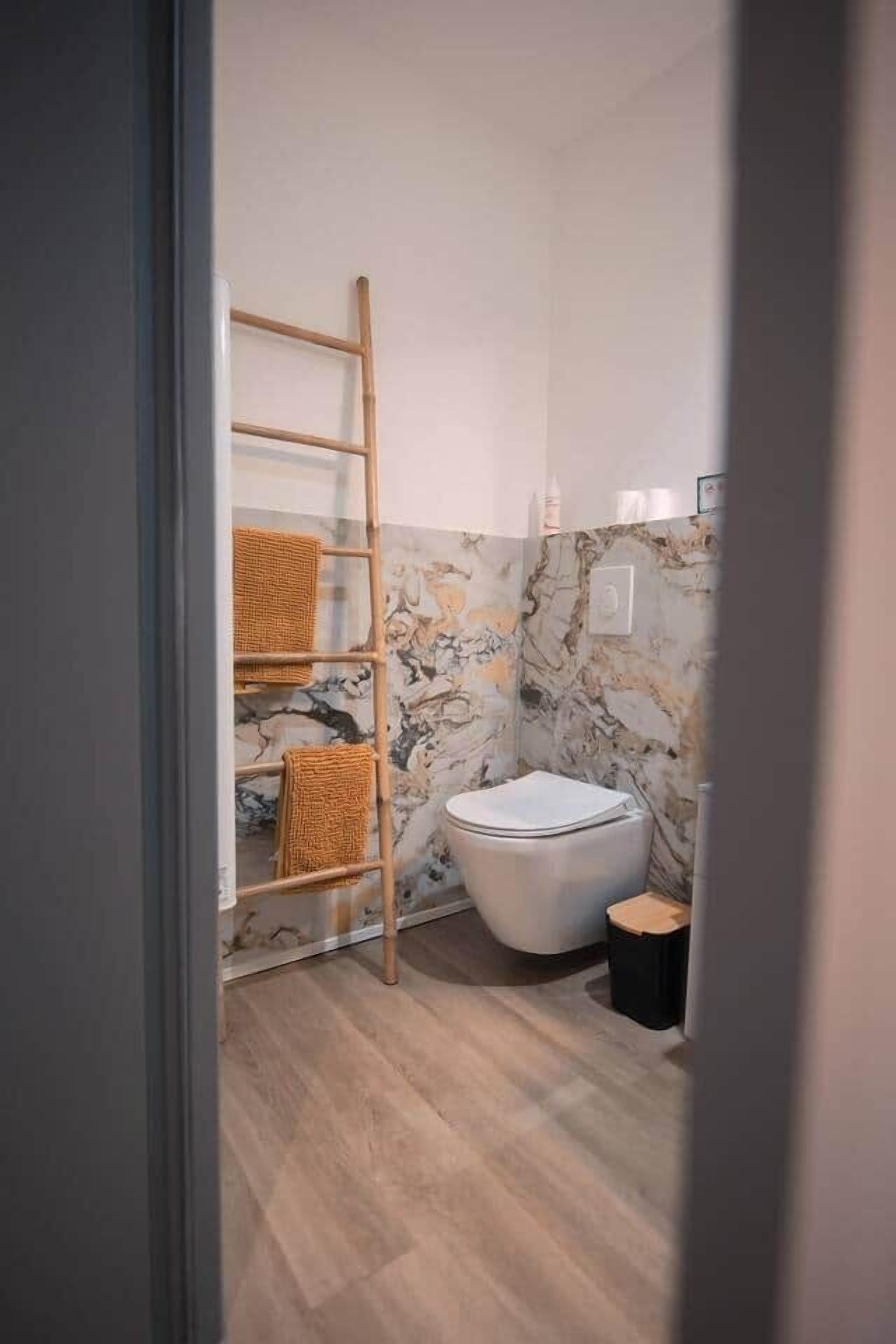 A bathroom with a marble wall, a toilet, a wooden ladder, and a small stool.