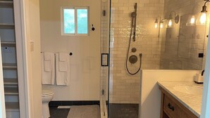 A modern bathroom with a glass shower enclosure, a white toilet, and a wooden vanity with a marble countertop. - Wine Country Home (Napa)