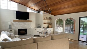 A modern living room with a fireplace, a large sofa, and a television mounted on the wall. - Wine Country Home (Napa)