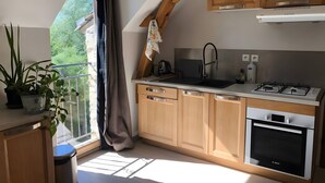 A kitchen with wooden cabinets, a gas stove, a sink, and a window with a view of greenery. - Apartment 'À L'Aujardière' with Shared Garden and Wi-Fi (Durtal)