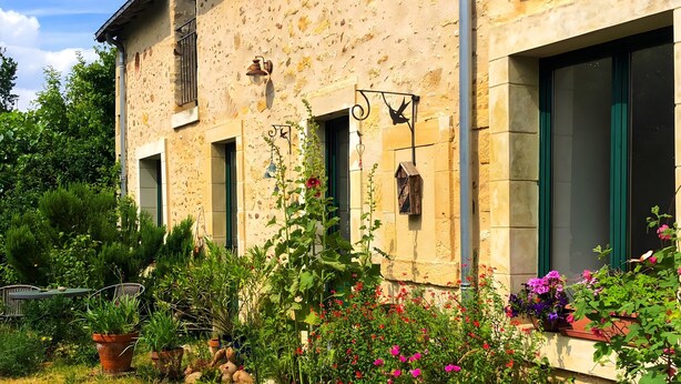 A rustic building with multiple windows, a garden with pink flowers, and a gravel path. - Apartment 'À L'Aujardière' with Shared Garden and Wi-Fi (Durtal)