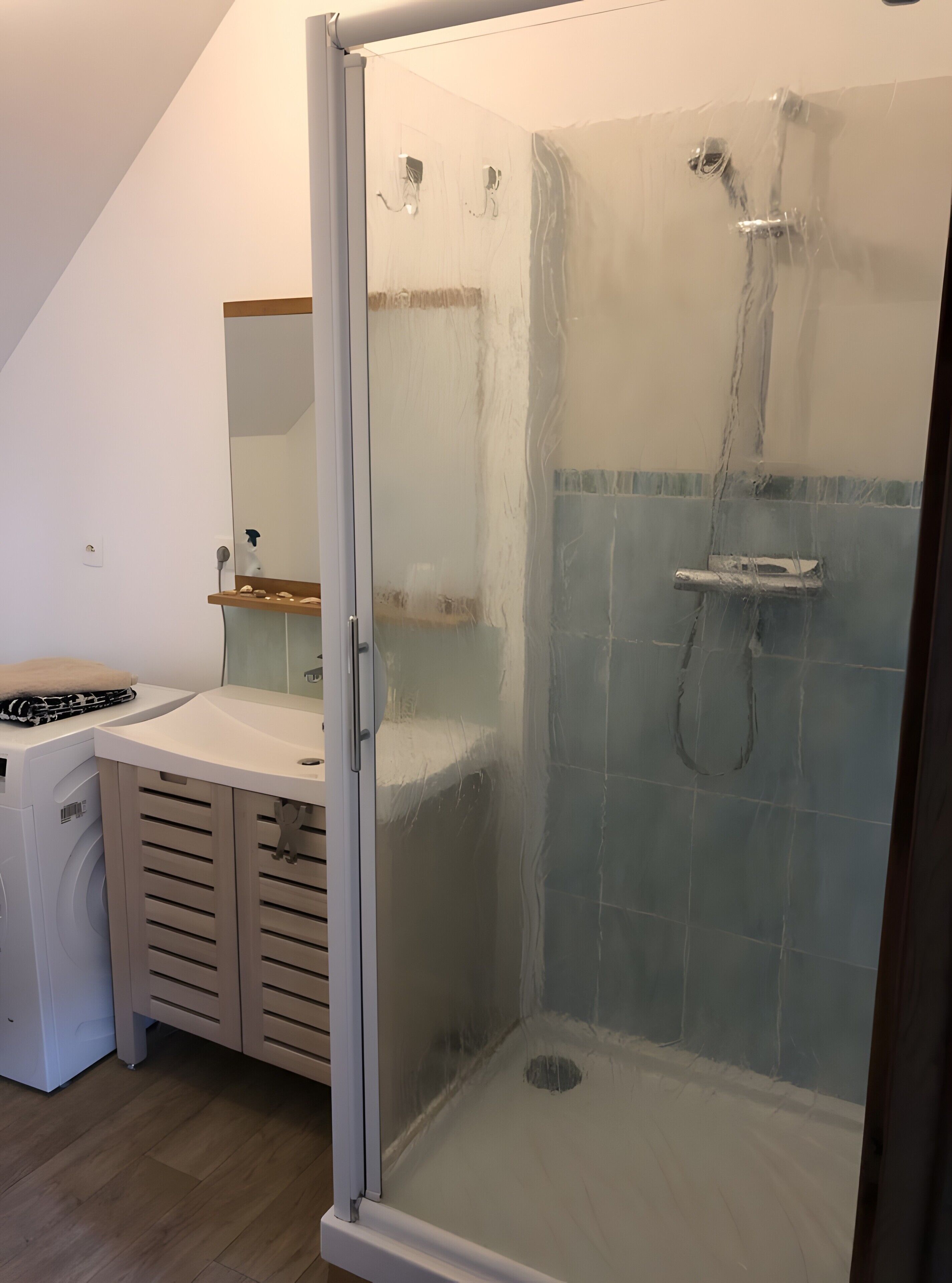Una ducha con puerta de cristal, un armario de madera y un espejo.