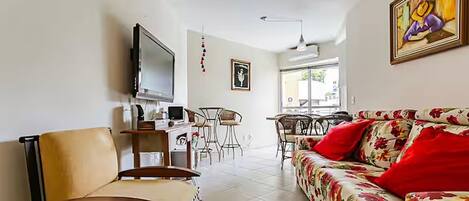 A living room with a sofa, a chair, a TV, and a dining area with chairs and a table.