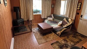 A cozy room with a brick floor, a sofa with patterned cushions, a wooden ceiling, and a window with curtains.