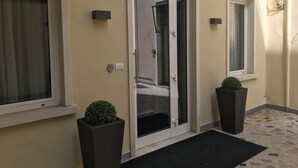 L'ingresso di un hotel con una porta in vetro, due piante in vaso e un tappetino nero.