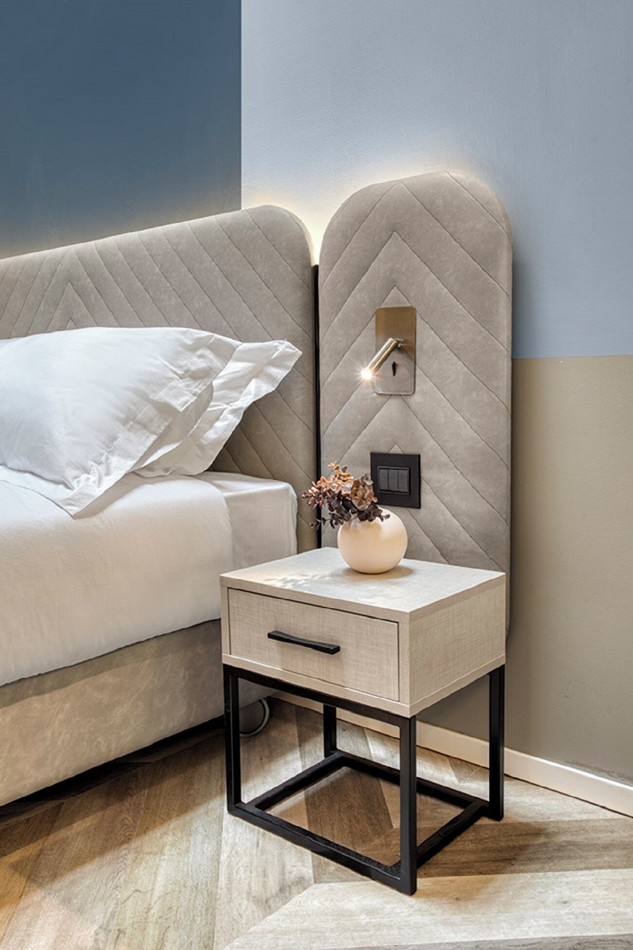 A modern bedroom with a bed, bedside table, and a wall-mounted light fixture.