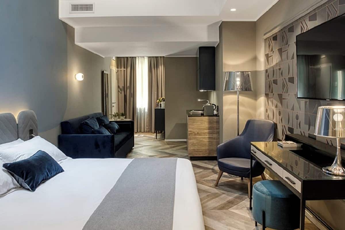 Una moderna camera d'albergo con un ampio letto, una scrivania, una sedia, una televisione e uno specchio.