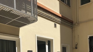 Un edificio con un patio piastrellato, due piante in vaso e una porta con un pannello di vetro.
