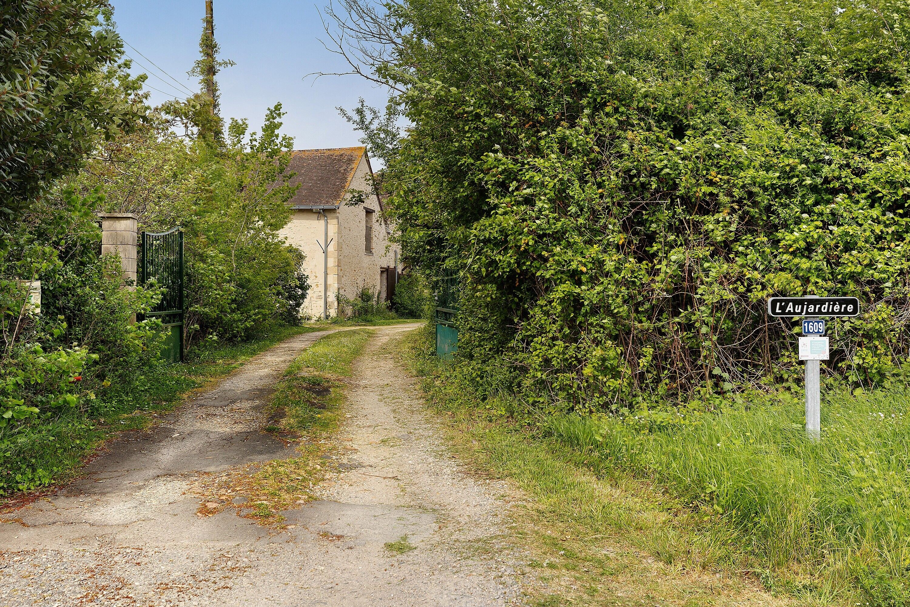 Un camino rural que conduce a un edificio con un letrero que dice 'L'Aujardiere 1609'.
