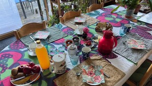 A table set with various items including a fruit bowl, a teapot, and a red kettle, with a colorful tablecloth and chairs around. - Guest Room 'Cocon' with Shared Garden and Wi-Fi (Durtal)