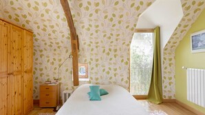 A bedroom with a bed, wooden wardrobe, a radiator, a window with curtains, and a wall with leaf-pattern wallpaper. - Guest Room 'Cocon' with Shared Garden and Wi-Fi (Durtal)